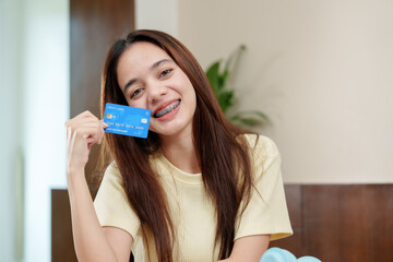 Happy young shopper with braces points to her credit card, excited about her online finds.Content...