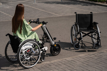 Woman in wheelchair with assistive device for manual control next to classic wheelchair. Electric handbike. 