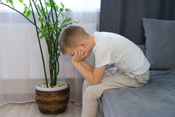 One sad little boy sitting in despair, alone at home on the sofa. Anxiety and stress. Concept of...