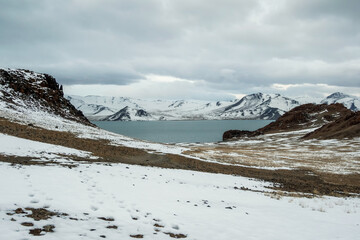 Fototapeta na wymiar Blue winter lake and snow mountains. Dirt road to the lake is covered with snow.