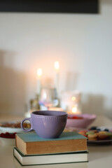Plate of pastel macarons, cookies and chocolate, cup of tea of coffee, glass of bubble water, various berries, books and accessories on the table. Selective focus, pastel colors.