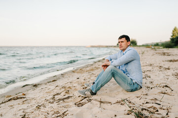 Portrait of stylish male enjoying amazing view. The handsome man joyfully walks near sea and looks at side. Young traveler man sitting in beach ocean and enjoying summer day on vacation. Side view.