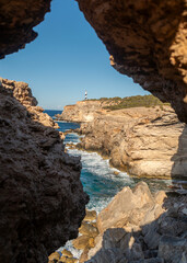 Punta Moscarter lighthouse seen through a rock hole in a cave near Portinatx, Sant Joan de Labritja, Ibiza, Balearic Islands, Spain