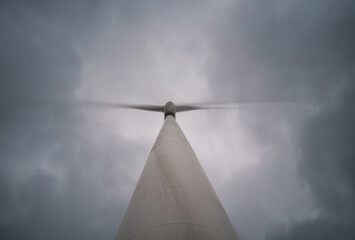 Under an overcast sky, a white wind turbine spins rapidly, churning out a steady stream of ene