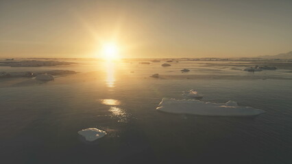 Antarctica ocean sunset light. Aerial drone view flight. Fastthe bright orange sun over the ocean surface covered ice, snow pieces and icebergs. Flying over the water. Copter.