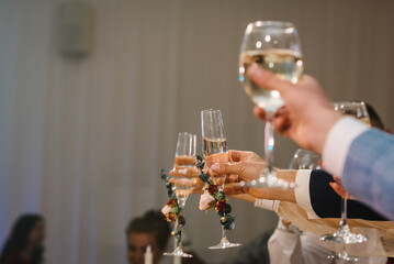 Cheers. Bride is holding glass of white wine outdoors and groom hold champagne. Wedding celebration...