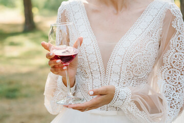 The bride is holding a glass of red wine outdoors. The girl has a beautiful dress and neckline...