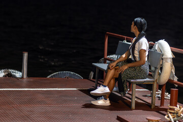 A young woman sits on an illuminated bench of a night ferry