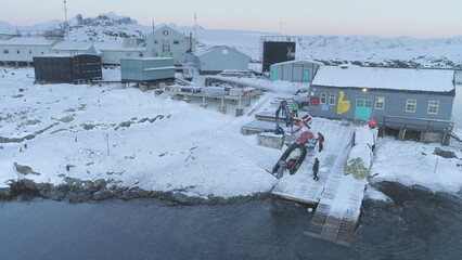 People work on pier of Antarctic polar station - Vernadsky. View of robotic arm pulls out boat....