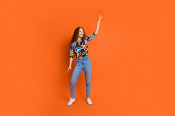 Photo of cheerful glad girl wear stylish print clothes rejoice have fun empty space isolated on vibrant orange color background