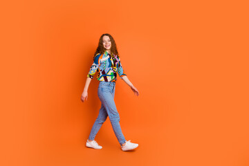 Photo of cheerful nice girl wear stylish print clothes walking empty space isolated on vivid orange...