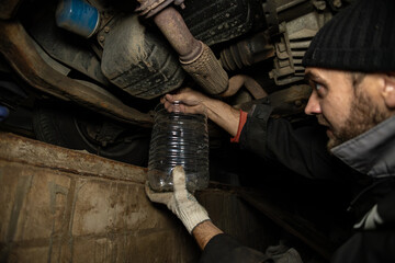 The mechanic removes the plug from the tank, draining the old engine oil from the engine. A...