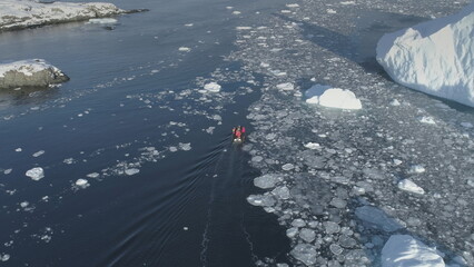 Polar explorers in motor boat sail between icebergs in Antarctica. Dangerous - people afraid get...
