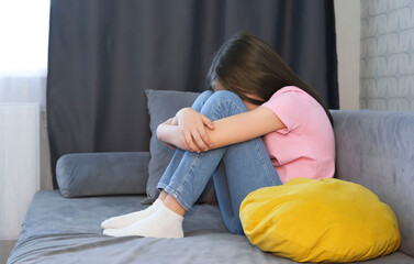 One sad girl sits in anxiety and despair on sofa at home. Concept of bullying, depressive stress or...