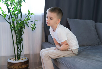 Little boy suffers from nausea in the living room. Child suffers from abdominal pain while sitting...