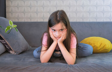 One sad girl sits in anxiety and despair on sofa at home. Concept of bullying, depressive stress or...
