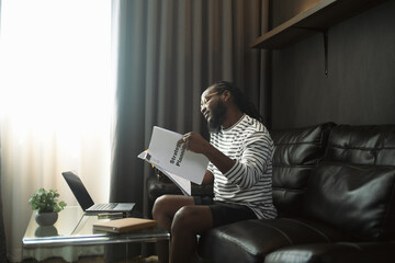 Busy African American man reading report or contract and talking on mobile phone at home