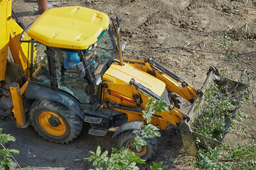 The bulldozer bucket removes green shrubs close-up, clearing the construction site from shrubs with...