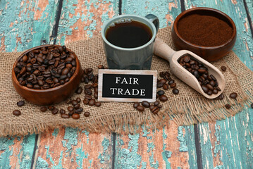 Fair Trade Kaffee:  Geröstete Kaffeebohnen und eine Tasse Kaffee mit dem Text Fair Trade auf einem...