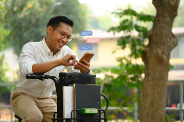 Pleased young businessman using mobile phone while sitting on a bicycle outdoor