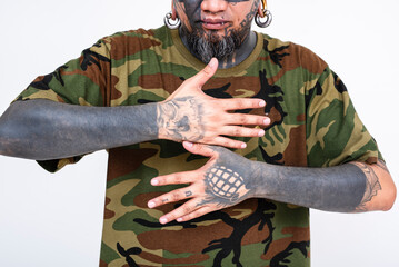 An asian man showing off full blackout sleeve tattoos on his arm, and grenade and skull on his hands. Set against a plain white backdrop.