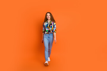 Photo of cute cheerful girl wear trendy print clothes going moving isolated on vivid orange color...