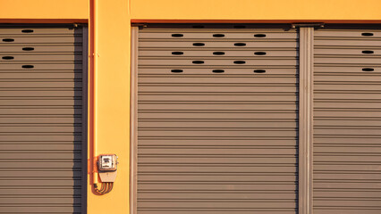 Roller shutter entrance door with electric meter and electrical conduit pipe in front of rental shophouse building