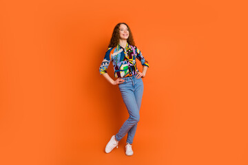 Photo of adorable cheerful girl wear stylish print clothes look empty space isolated on vivid orange color background