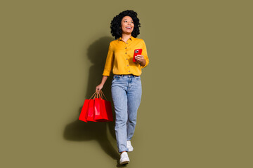 Full size photo of nice young woman phone bags walk empty space wear yellow shirt isolated on khaki color background