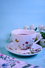 porcelain cup on a saucer with aromatic tea on a blue background with white flowers