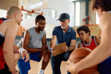 Basketball coach analyzing game plan with his players on court.
