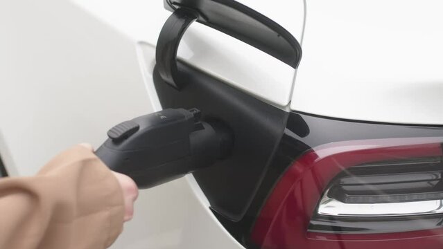 Hand-held shot of a woman's hand charging an electric car at an outdoor charging station against the background of a business center of a European street. Zero emission vehicle.
