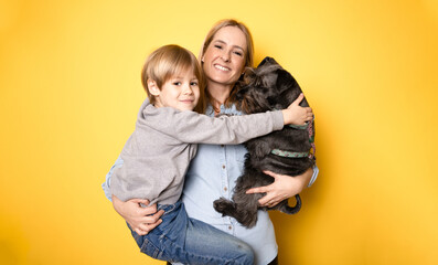 Happy mother with her son and schnauzer dog standing isolated on yellow background.