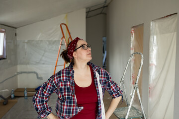 A woman with her hands resting on her side inspects the walls while renovating his premises, assessing the amount of work. High quality photo