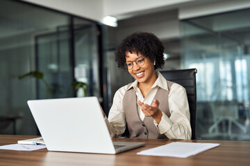 Happy professional young African female hr manager, smiling business woman in office wearing earbuds looking at laptop computer having hybrid conference work meeting or remote job interview.