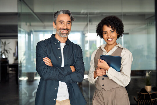 Two diverse business partners, employees or executives standing in office looking at camera. Man and woman sales managers, company workers, consultancy professionals posing for corporate portrait.