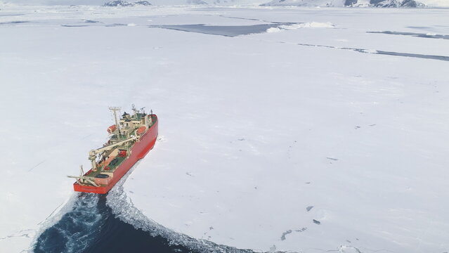 Icebreaker breaks through pack ice on its way. Red Nuclear icebreaker clears its pass in Antarctica. Vessel navigating: Aerial view. Featuring Research Boat slicing through Southern Ocean's ice.