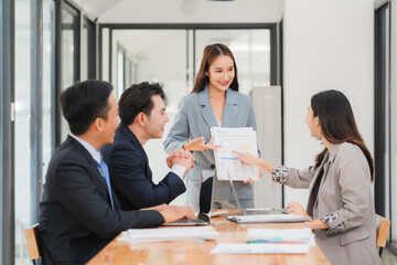 Group of businesspeople are sitting around a table in a business setting. They are all smiling and seem to be enjoying each other's company