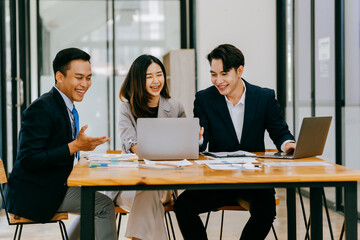 Group of businesspeople are sitting around a table in a business setting. They are all smiling and seem to be enjoying each other's company
