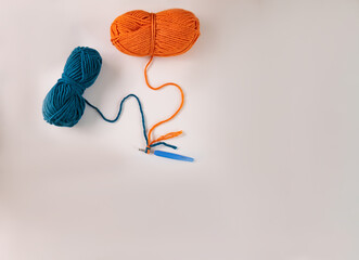 two balls of orange blue thread for knitting or crocheting with blue hook on a light background