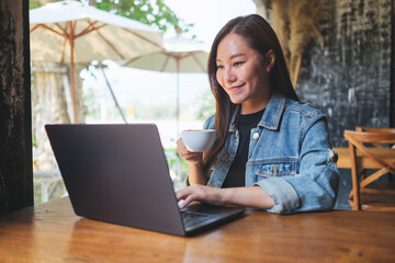 Portrait image of a young woman drinking coffee while working on laptop computer in cafe - 796411882