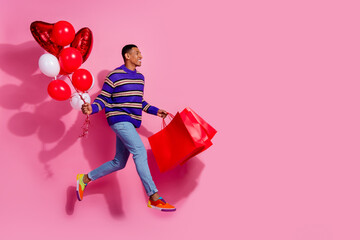 Full length photo of positive dreamy guy dressed striped pullover running holding bargains balloons...