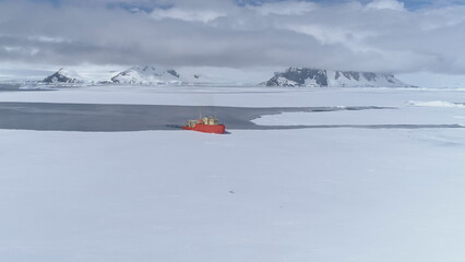 Red icebreaker breaks ice in Antarctica making its way: Aerial flight view. Vessel navigating Antarctic waters. Featuring the Laurence M. Gould Research Boat slicing ocean. Dramatic break pack ice.