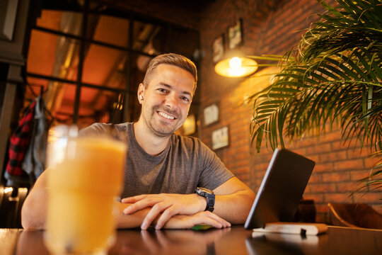 Portrait of a young entrepreneur sitting at cafe with earbuds and tablet, smiling at the camera.