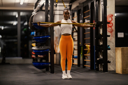 A slim black sportswoman is stretching resistance band at the gym.
