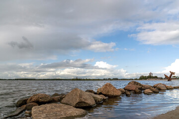 Fototapeta na wymiar Boulders in the water of the Wolderwijd with the monument to Allied airmen near Harderwijk, Netherlands in the background