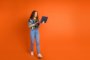 Photo of cheerful pretty girl user wear stylish clothes going empty space isolated on vivid orange color background