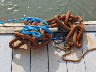 A closeup view of some blue nylon rope and some large rusty links forming a piece of chain on a...