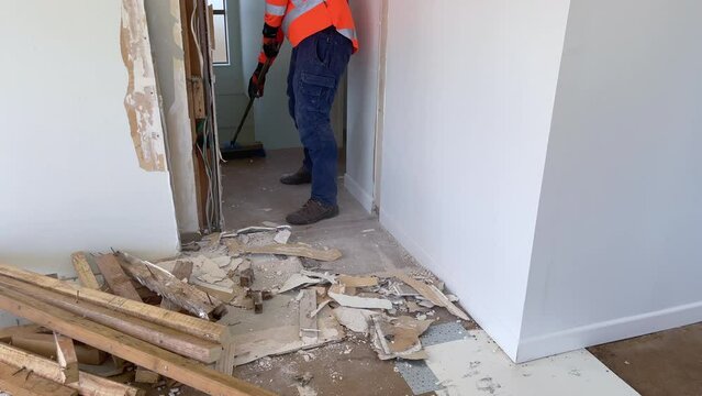 Worker in high-visibility clothing sweeps up debris after the demolition of a plasterboard and timber framed wall