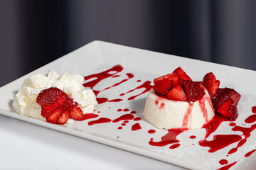 Panna cotta with cream and strawberries in rectangular white plate on white gray background